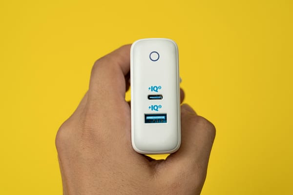Carregador compacto GaN com conectores USB fotografado próximo a dispositivo eletrônico